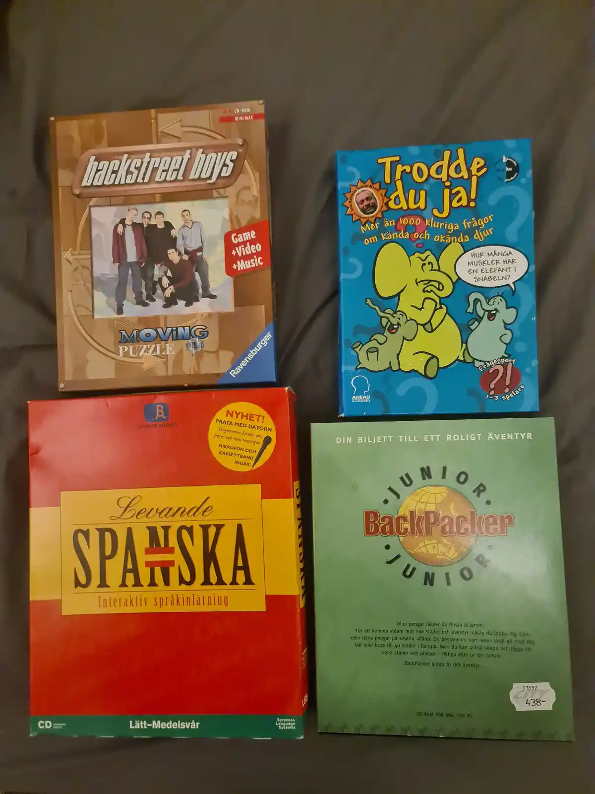 Four vintage Swedish CD-ROM educational and entertainment software boxes are arranged on a dark fabric surface. The top-left…