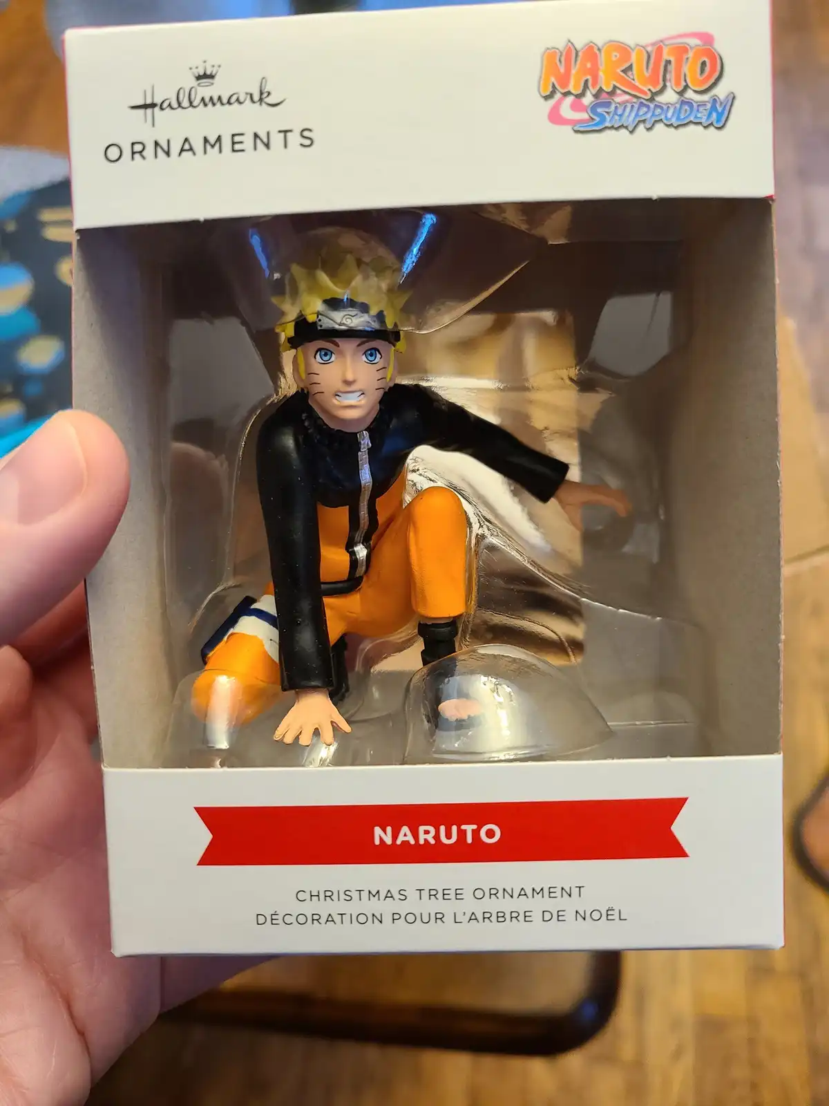 A hand holds a Hallmark Christmas ornament box featuring the anime character Naruto from Shippuden. The figurine inside is…