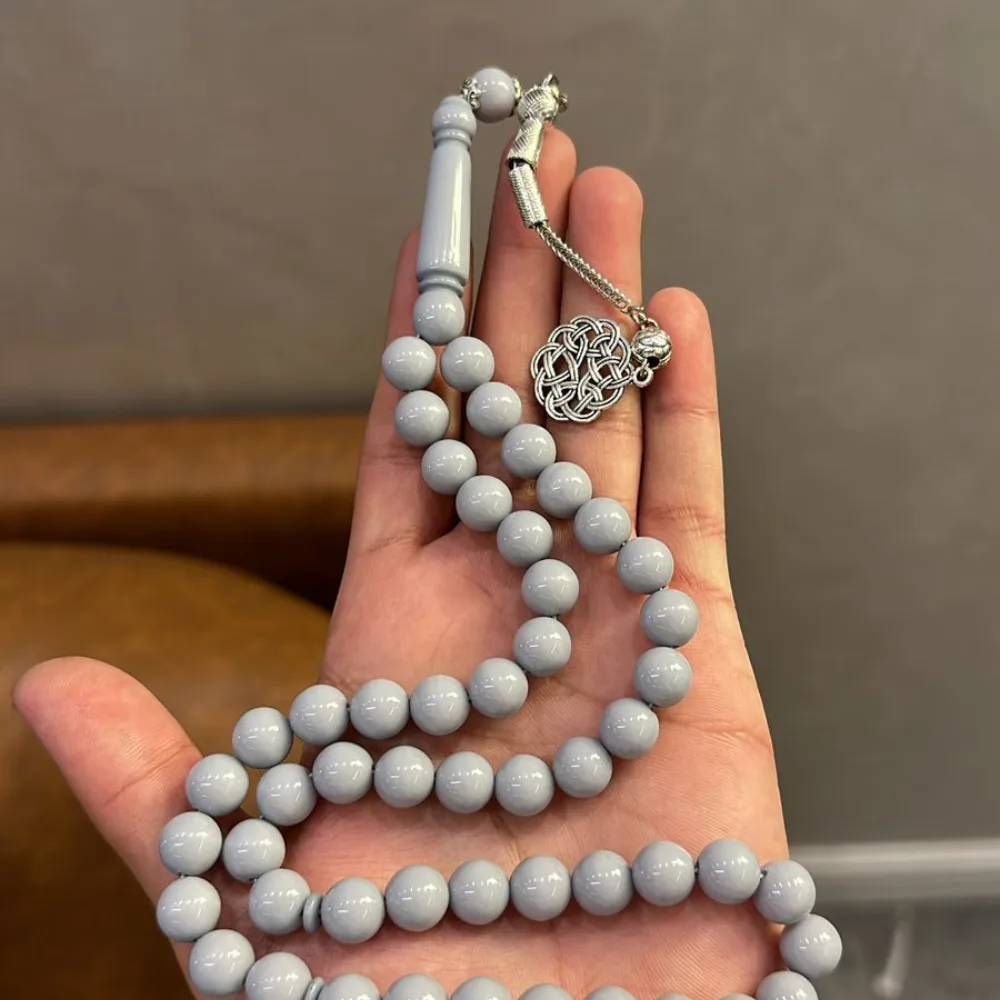 A person's open palm holds a long string of light gray prayer beads with a silver-colored metal clasp and decorative knot…