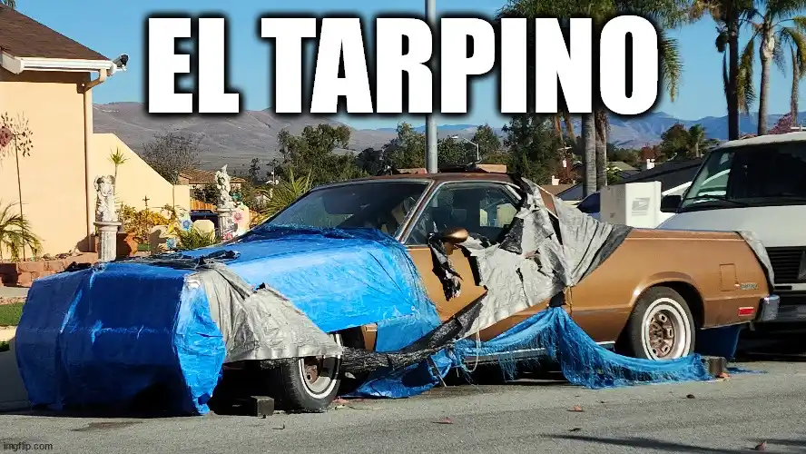 A brown car is partially covered with blue and gray tarps, with the tarps torn and frayed, suggesting a makeshift repair or…