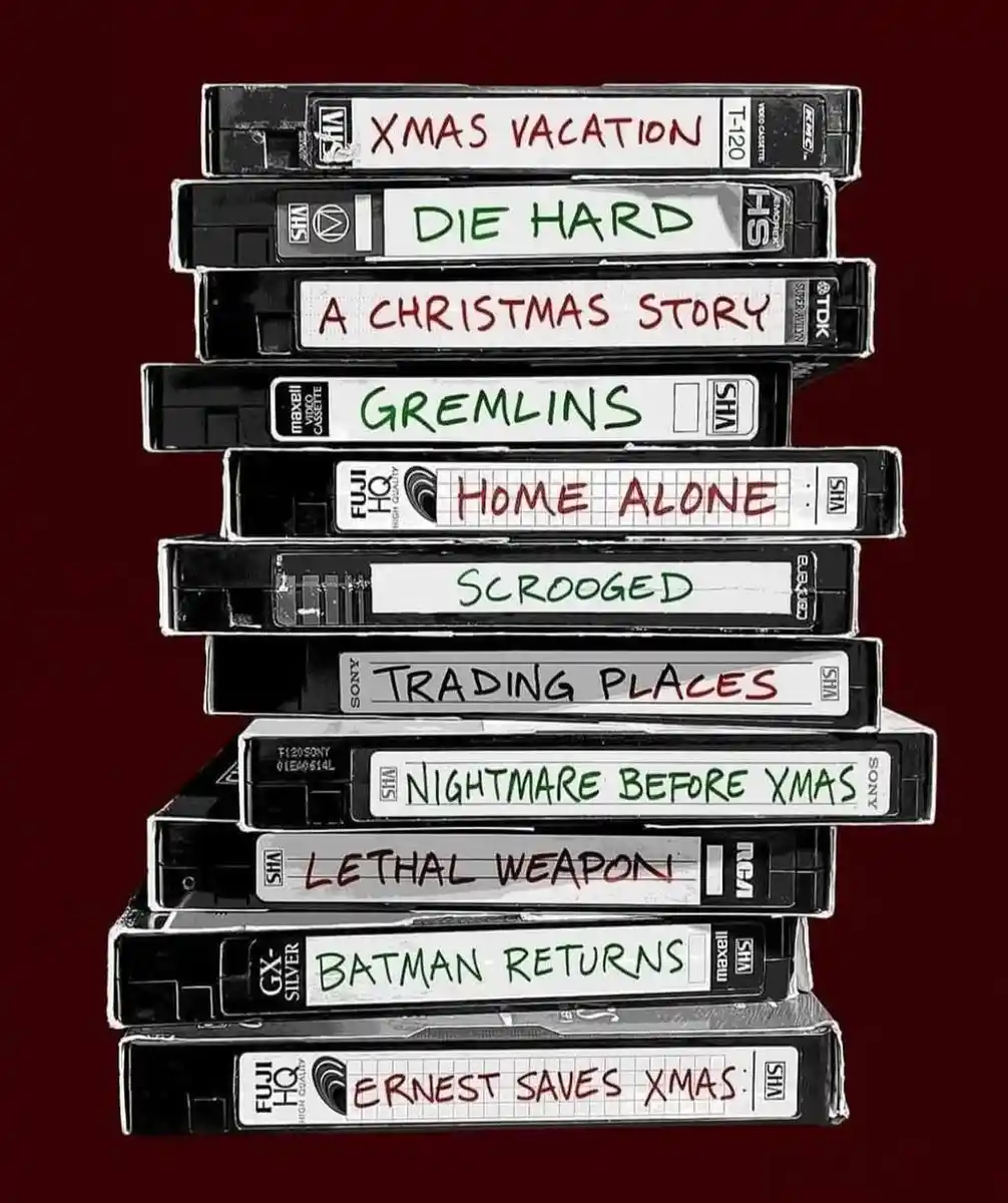 A stack of VHS tapes with handwritten titles like 'XMAS VACATION', 'DIE HARD', 'A CHRISTMAS STORY', 'GREMLINS', 'HOME…