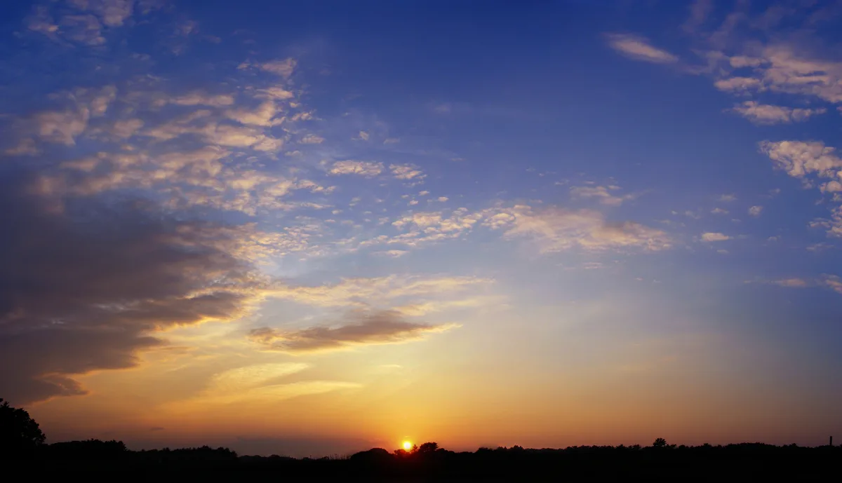 A serene sunset photo with the sun low on the horizon, casting orange and yellow hues across the sky, with scattered clouds…