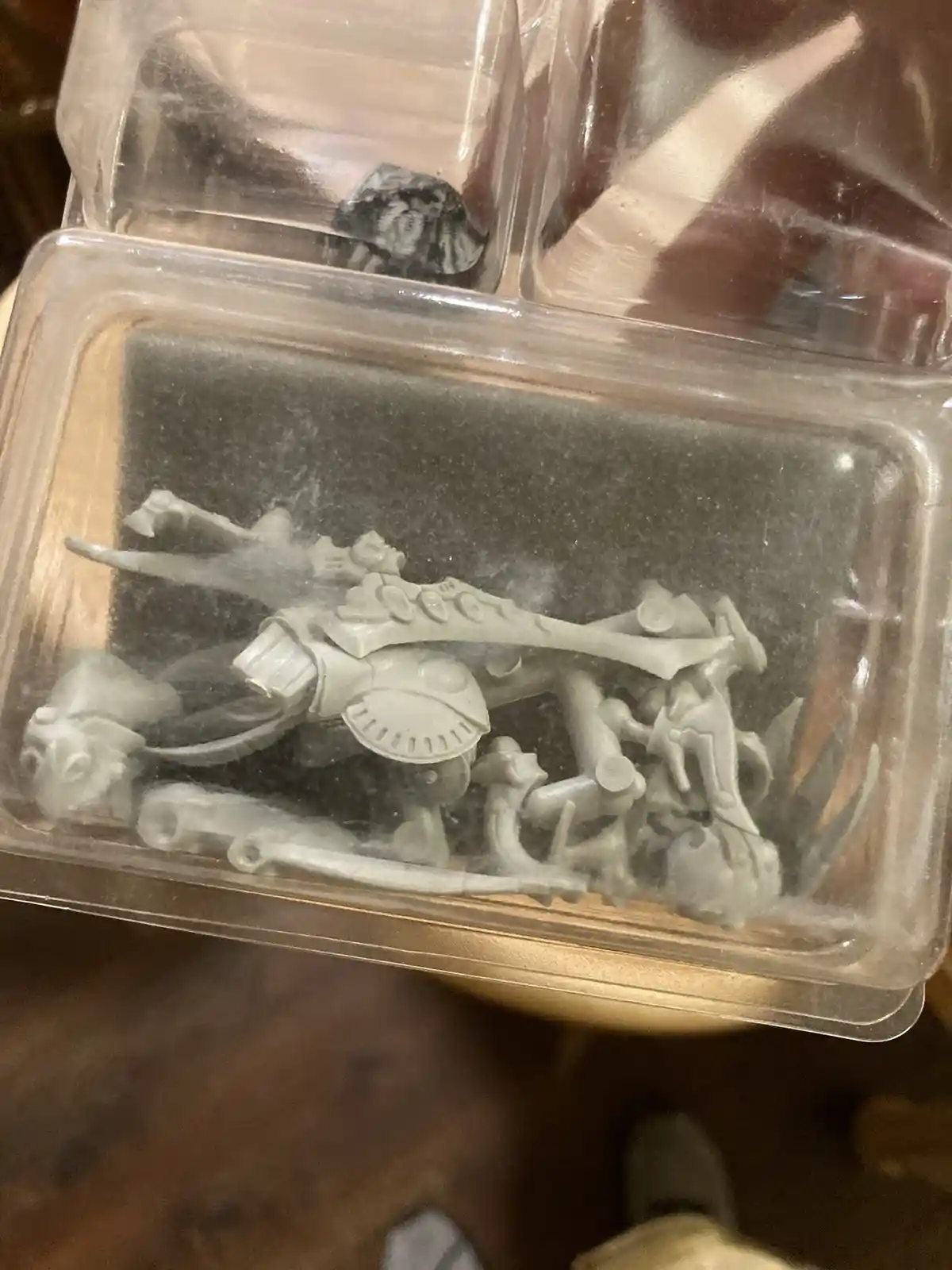 A close-up photo shows a clear plastic blister pack containing a disassembled, unpainted model kit with numerous gray…