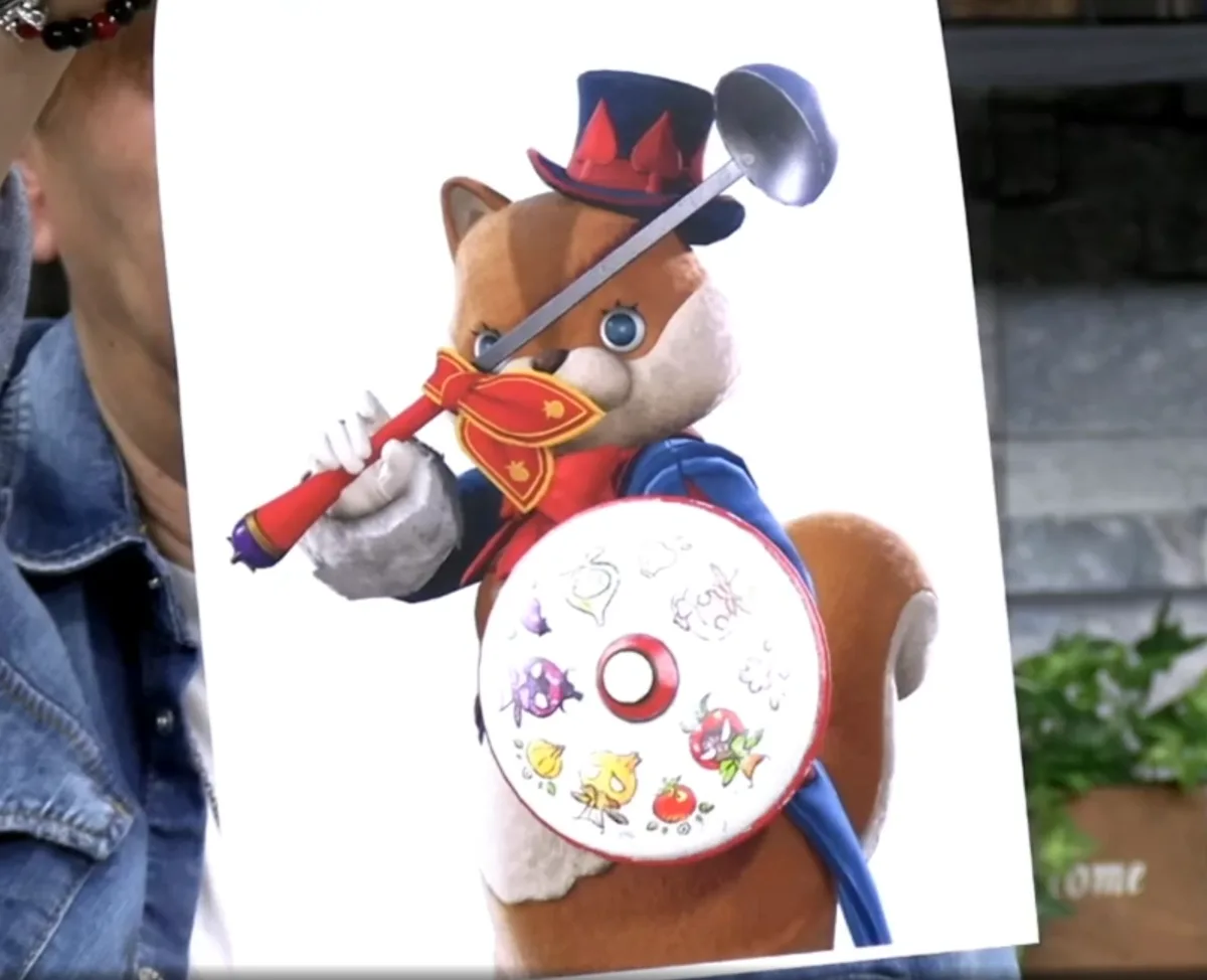 A person holds up a printed image of a cartoon fox character dressed as a chef, wearing a top hat with red spade symbols…