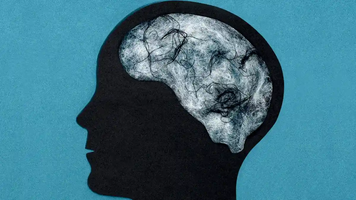 A black silhouette of a human head in profile against a blue background, with a brain inside showing tangled, messy black…
