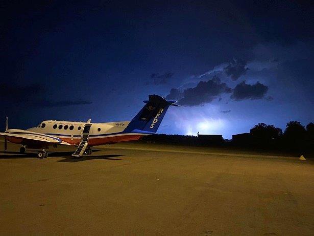 A small private airplane, with 'REDS' written on its tail, sits parked on a tarmac at night. Behind it, a dramatic lightning…