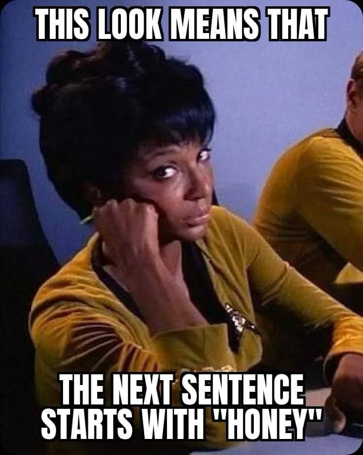 A woman in a yellow Star Trek uniform stares intently with her hand near her cheek, conveying a warning or expectation. The…