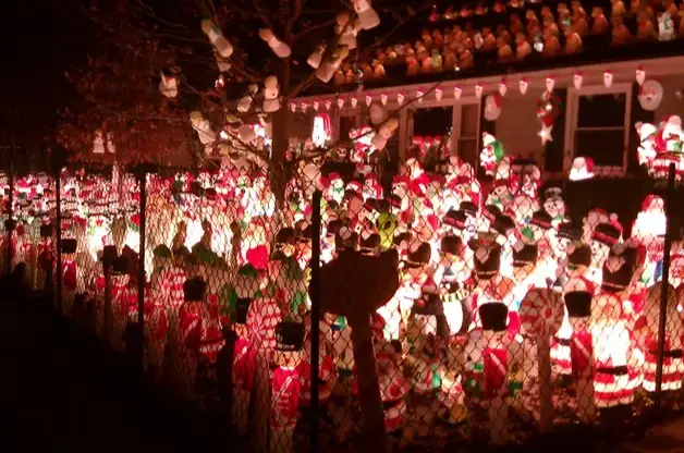 a nighttime photo of a house and yard densely covered with illuminated christmas decorations, including santa claus…