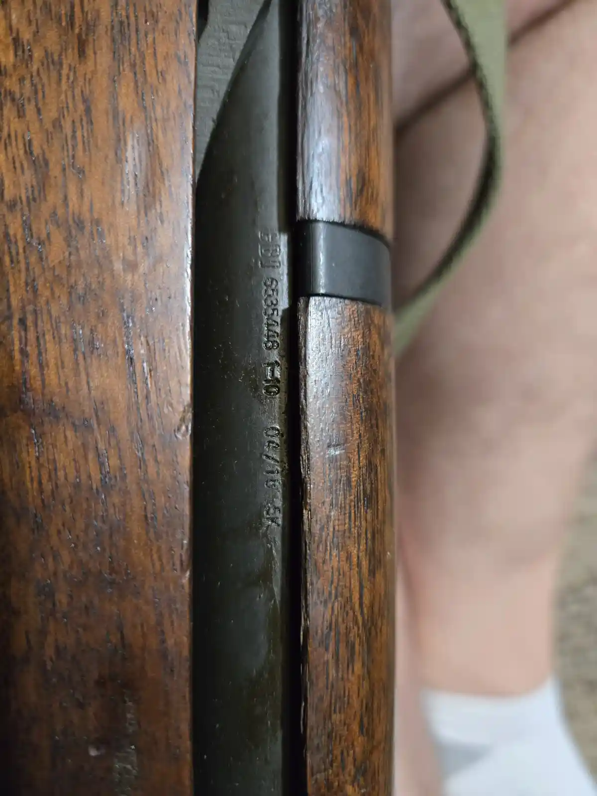 A close-up photo shows the serial number and markings engraved on the metal receiver of a wooden-stocked rifle, held by a…