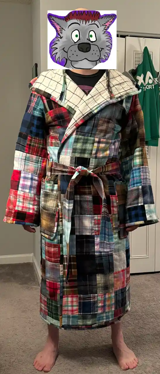 A person stands barefoot in a full-length robe made from a patchwork of many different colored plaid fabrics, with their…