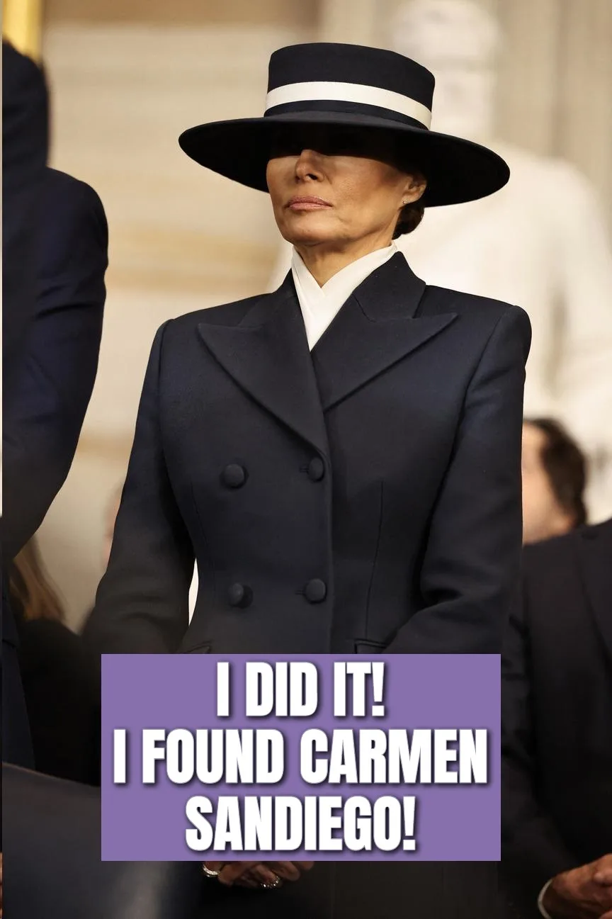 A woman wearing a wide-brimmed black hat with a white band and a dark navy double-breasted coat stands with a serious…