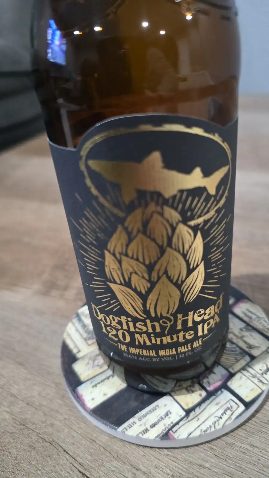 A close-up of a brown glass beer bottle with a black and gold label featuring a shark above a hop cone, sitting on a cork…