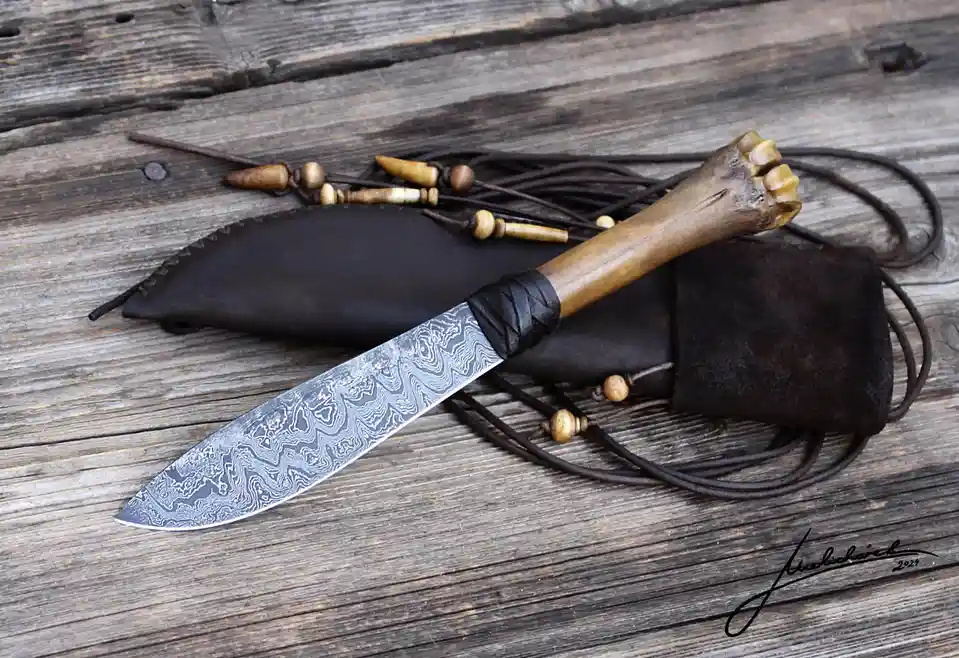 A handmade knife with a distinctive damascus steel blade and a handle crafted from a bone-like material rests on a weathered…