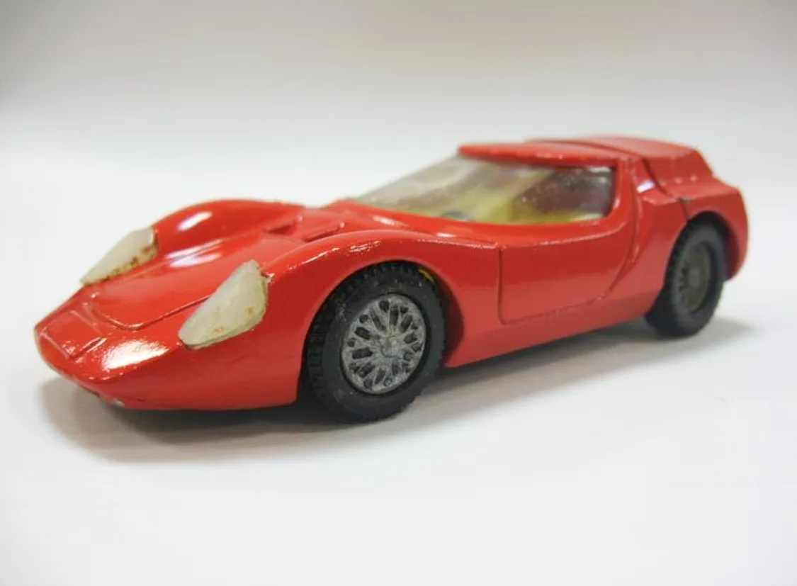 A red toy sports car with two white, rounded protrusions on its front resembling eyes, set against a plain white background…