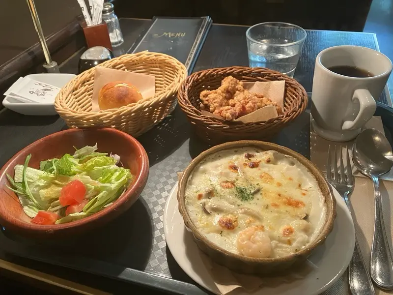 a table setting with a baked dish in a ceramic bowl, a side salad in a wooden bowl, fried chicken in a wicker basket, a…