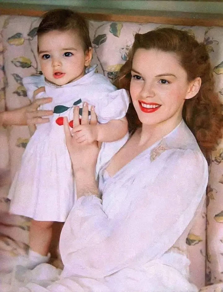 A vintage photo shows a smiling woman in a white dress holding a young child in a matching white dress with cherry…