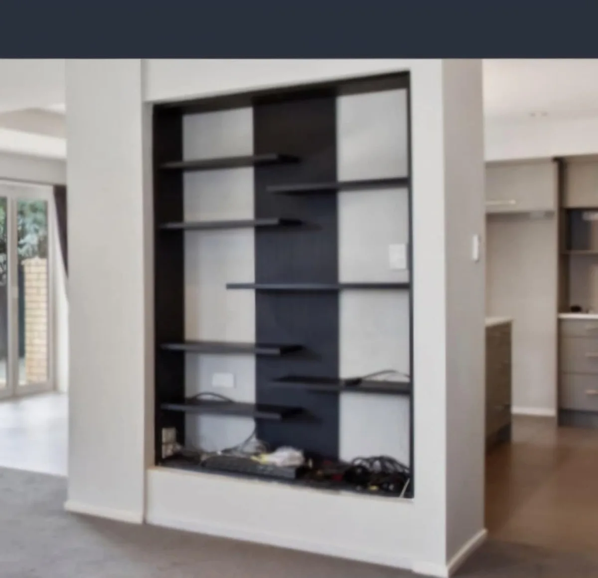 A modern, built-in wall unit with black shelves and white panels is shown, but the bottom shelf is cluttered with tangled…