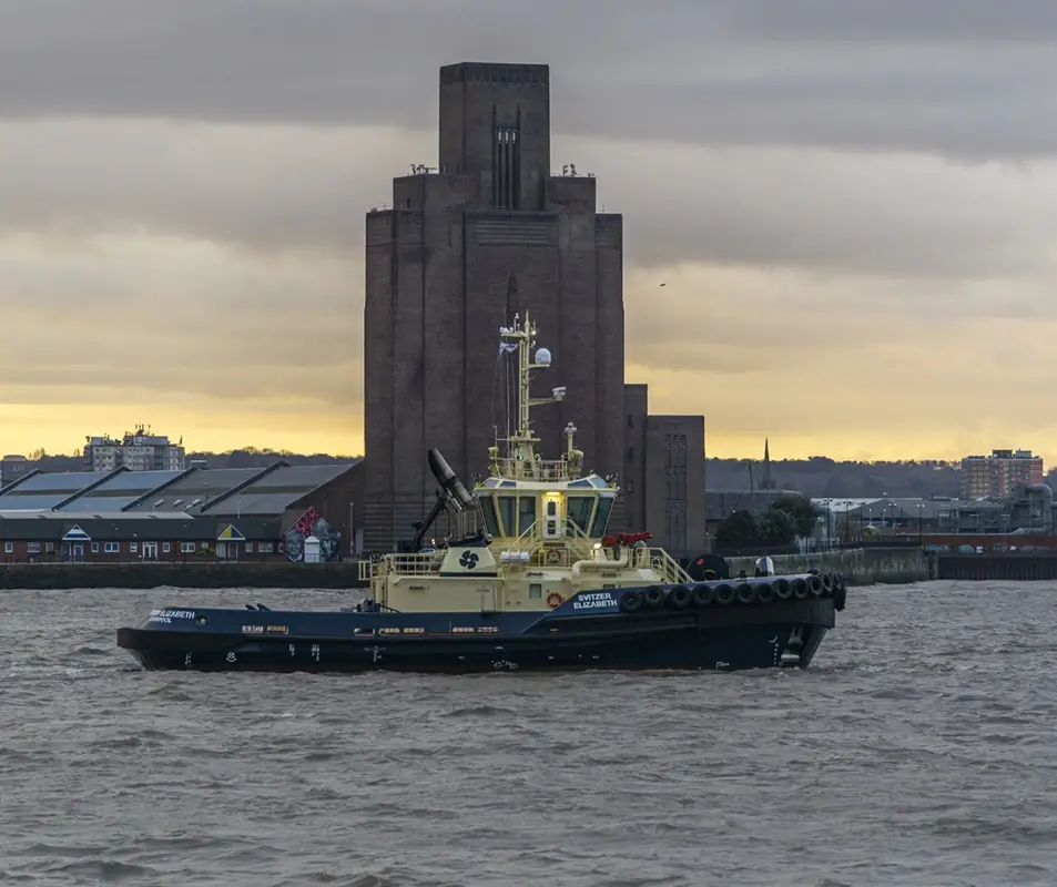A yellow and black tugboat named 'Switzer Elizabeth' sails on choppy water with the iconic Tate Modern building in the…