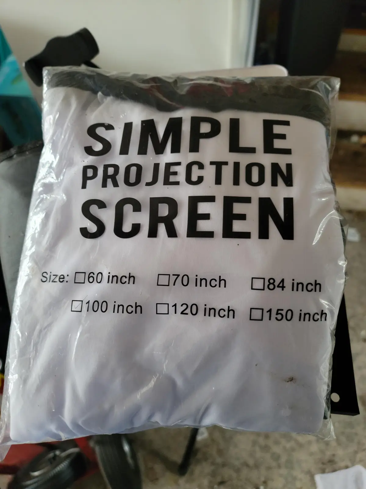 A white projection screen packaged in clear plastic, labeled 'SIMPLE PROJECTION SCREEN' with size options. The '100 inch'…