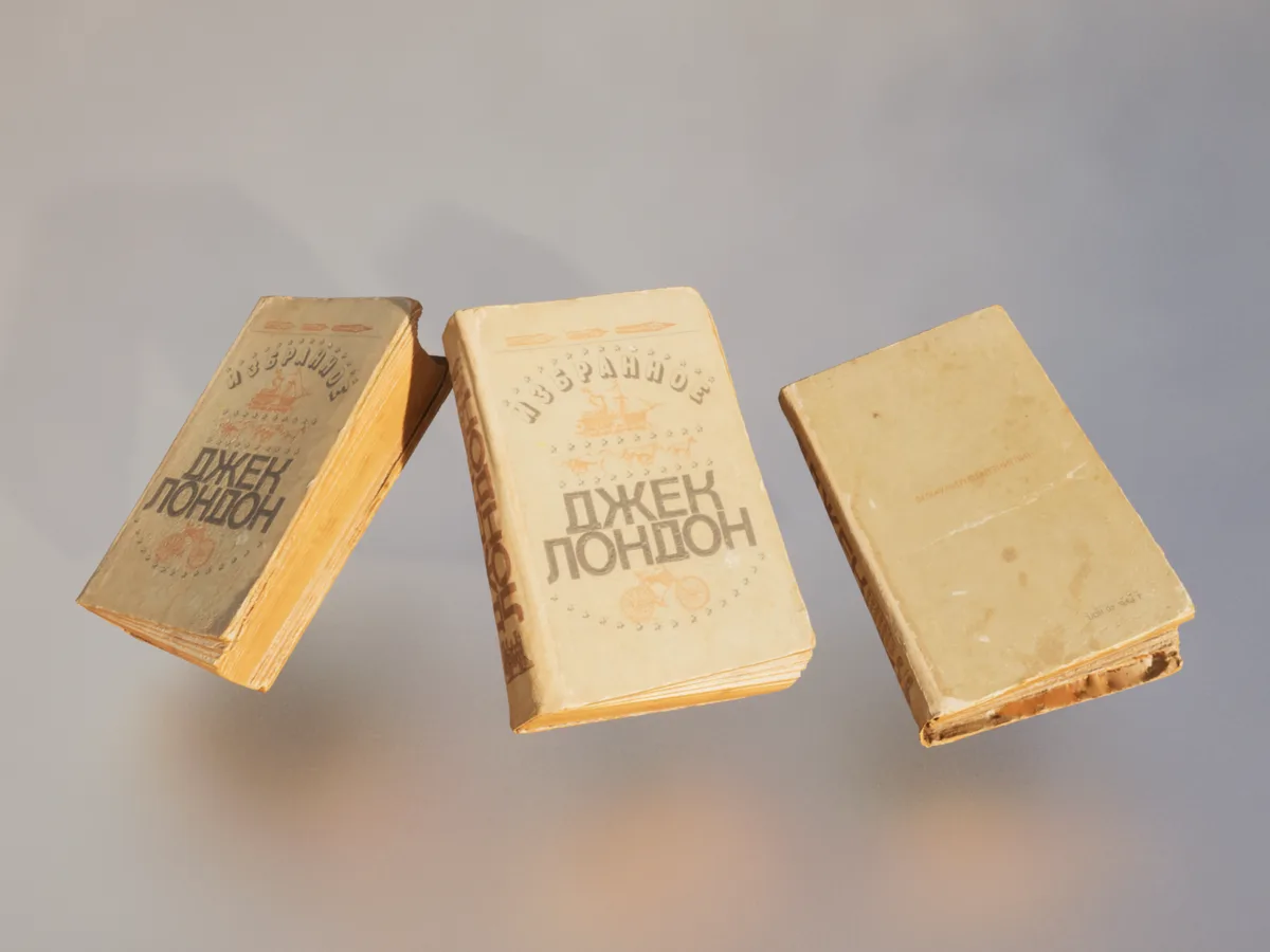 Three old, yellowed books with Cyrillic text 'Избранное ДЖЕК ЛОНДОН' float against a plain gray background. The books show…