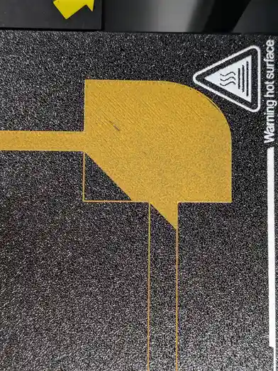 A close-up of a black textured surface with a yellow arrow pointing right, next to a white triangular warning symbol with…