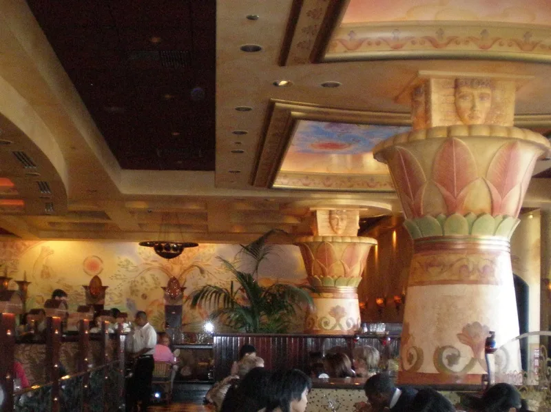 the image shows the interior of a restaurant with large, ornate pillars decorated with painted faces resembling ancient…