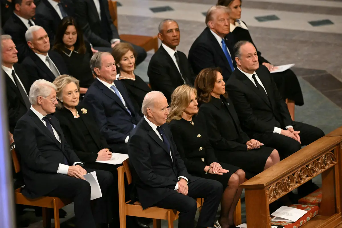 A photo of several former U.S. presidents and their spouses seated in a formal, solemn setting, dressed in black. President…