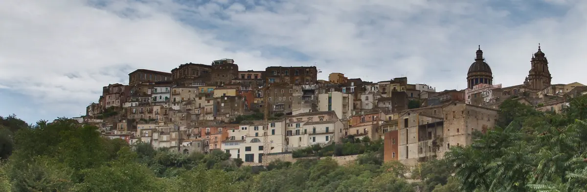 a panoramic view of a densely packed, historic hillside town with terracotta-roofed buildings, a prominent domed cathedral…