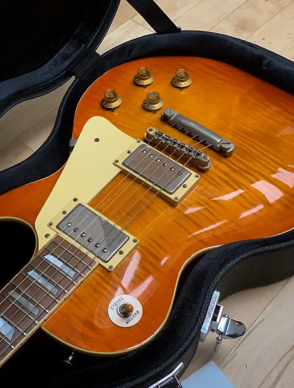A close-up photo of a sunburst electric guitar resting inside its black case, showing its pickups, control knobs, and…