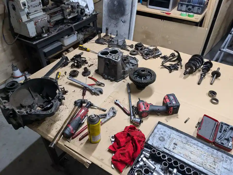 A cluttered workbench is covered with disassembled engine parts, tools like wrenches, sockets, and impact guns, and a red…