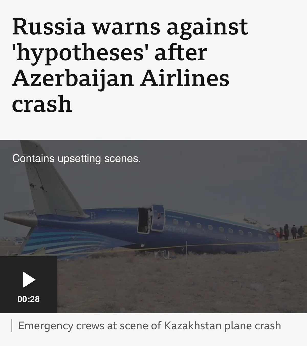 The image shows a crashed blue and white airplane on a barren field, with emergency crews visible in the distance. The…