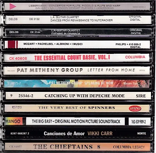 A vertical stack of cassette tapes with visible labels showing album titles and artist names like 'The Essential Count…