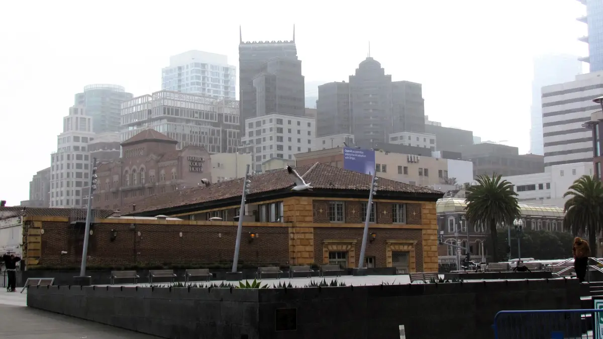 A foggy cityscape featuring the Harbor Court Hotel and modern skyscrapers, with a seagull flying in front of a brick…