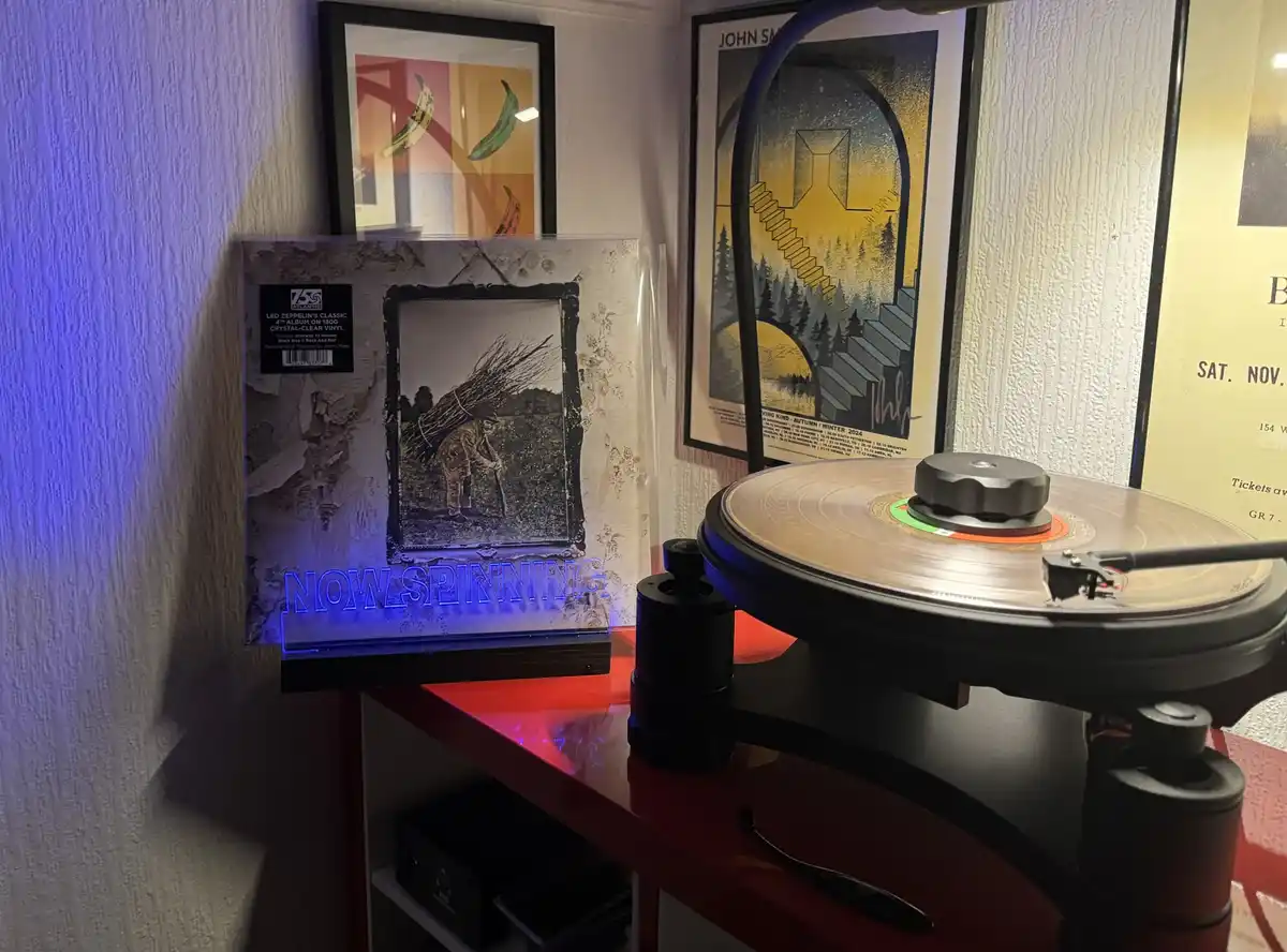A vinyl record player spins a gold-colored record on a red shelf, next to a Led Zeppelin 'Led Zeppelin IV' album cover with…