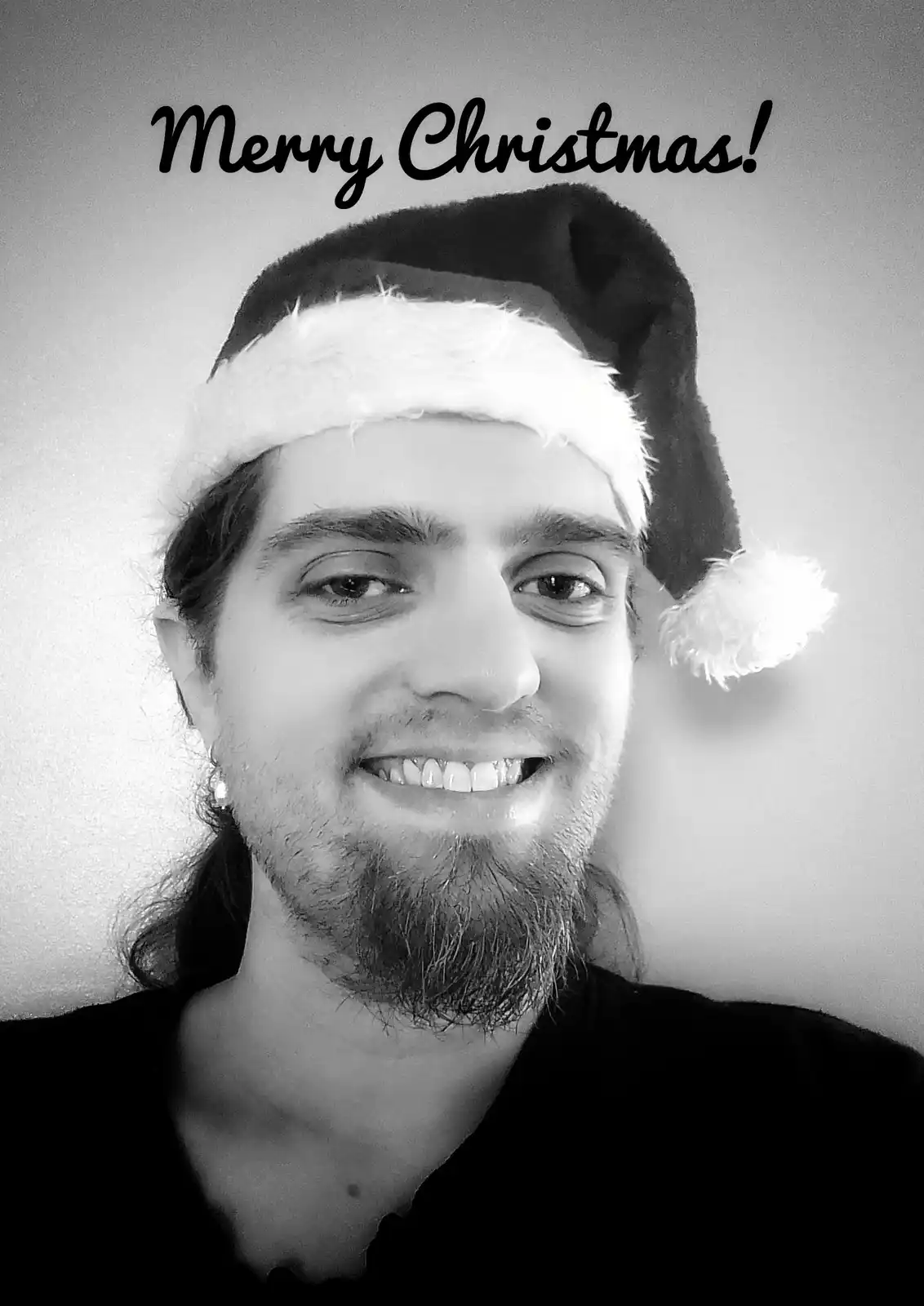 A black-and-white selfie of a smiling man with a beard and long hair wearing a Santa hat, with the text 'Merry Christmas!'…