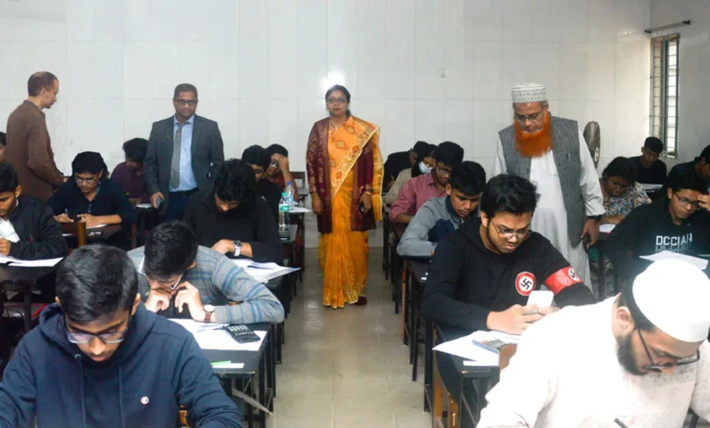 A photo of students taking an exam in a classroom, with one student in the foreground looking at his phone while wearing a…