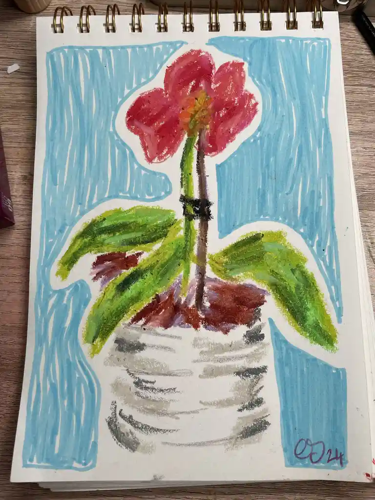 A child's crayon drawing on a spiral-bound notebook shows a red flower in a white pot with green leaves against a blue sky…