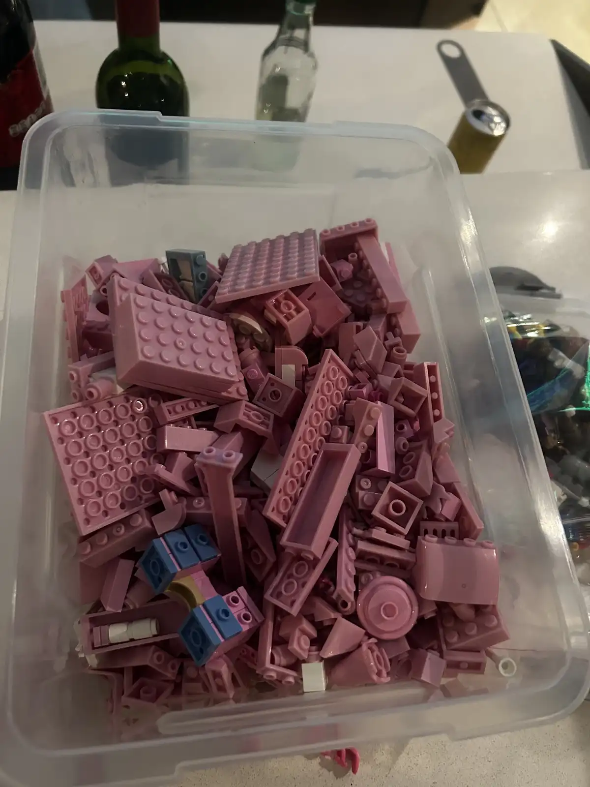 A clear plastic bin is filled with mostly pink Lego bricks of various shapes and sizes, with a few blue and white pieces…