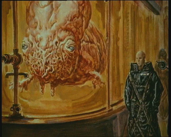 A bald man in a dark, textured robe stands beside a large, ornate glass tank containing a grotesque, fleshy, multi-eyed…