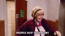 A woman in a maroon cardigan and beige hat stands in an elevator, repeatedly shouting 'people huv tae know!' as a man in a…