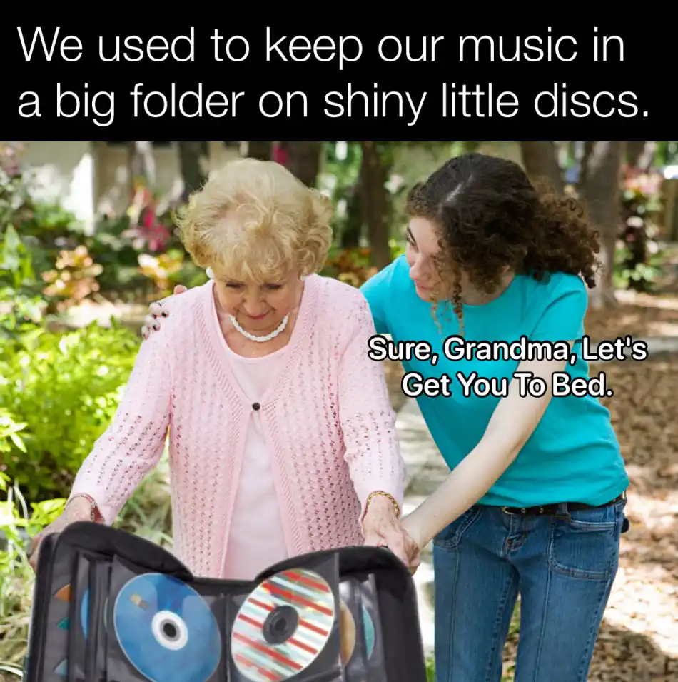 An older woman in a pink cardigan holds a black CD case filled with shiny discs while a younger woman in a blue shirt…