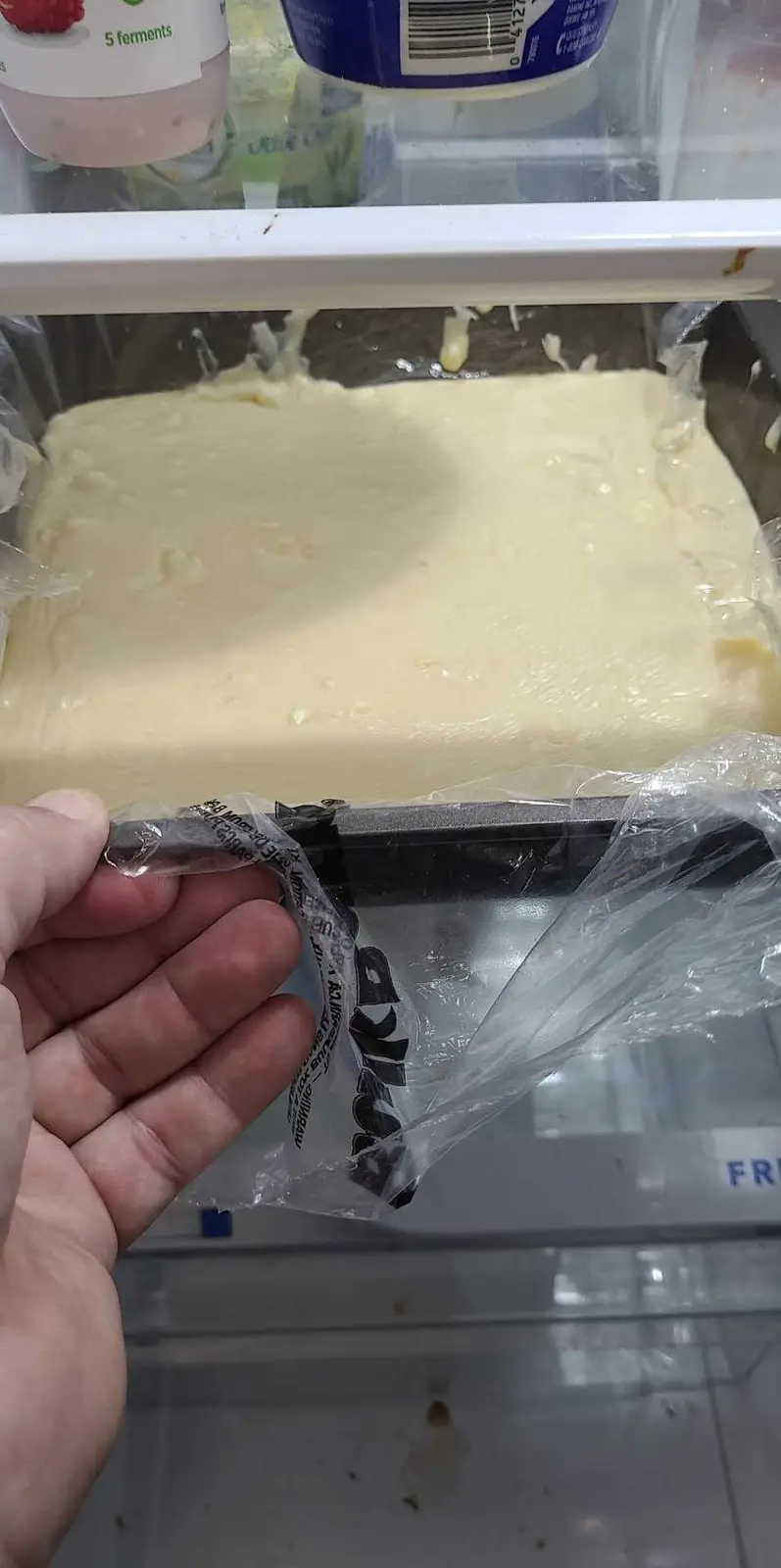 A hand holds a plastic bag with 'IKEA' branding, partially obscuring a large, messy, pale yellow substance in a freezer…