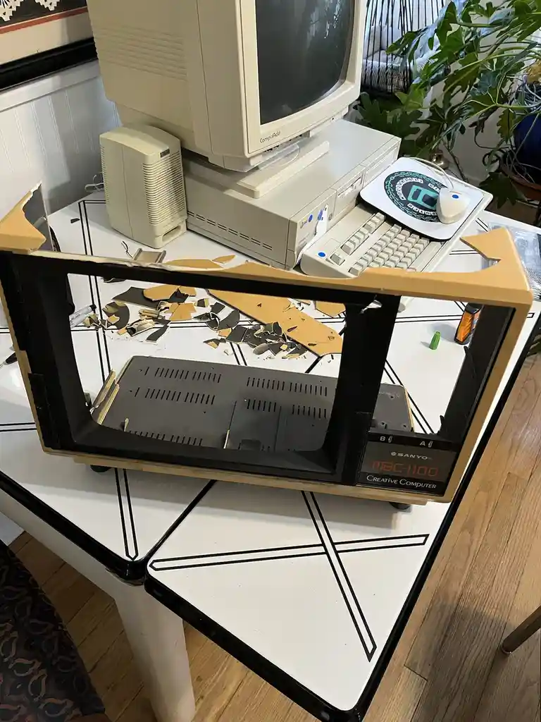 A Sanyo MBC-1100 Creative Computer, an old beige desktop computer, is shown with its front panel shattered and broken…