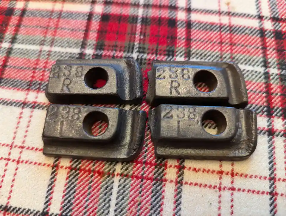 Four identical dark metal parts, each stamped with '238 R' or '238 L', are arranged in a two-by-two grid on a red, black…