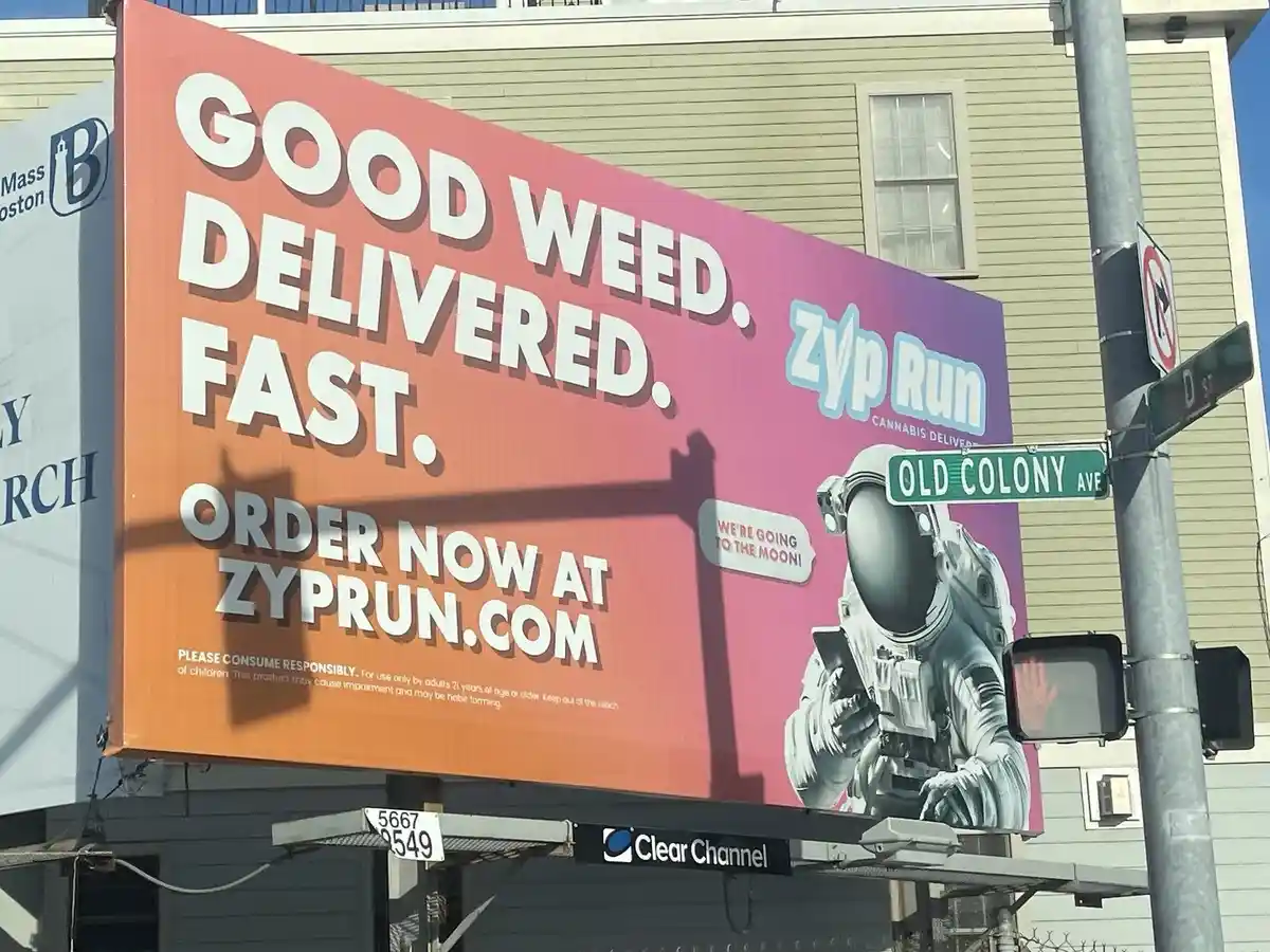 A large outdoor billboard for 'Zyp Run Cannabis Delivery' features a graphic of an astronaut holding a smartphone, with the…