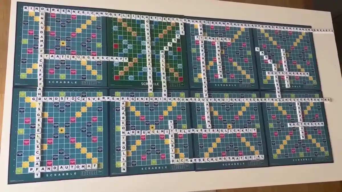 Eight Scrabble boards are arranged in a grid, forming a massive interconnected game. Long words like 'STAATSBÜRGERSCAFT'…