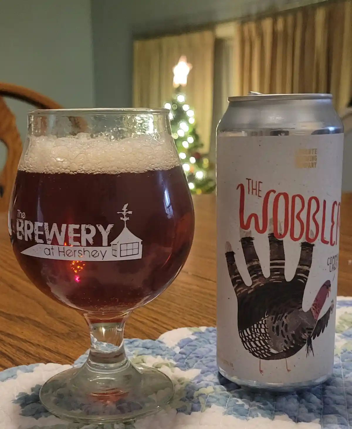 A beer can labeled 'The Wobbler' with a turkey illustration sits next to a glass of dark beer with a foamy head, both on a…