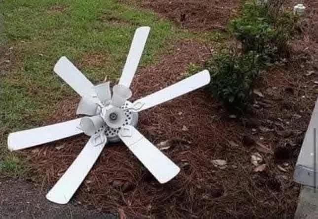 A white ceiling fan with five blades lies on its side in a yard with grass and mulch. The overlaid text reads 'i'm not lazy…