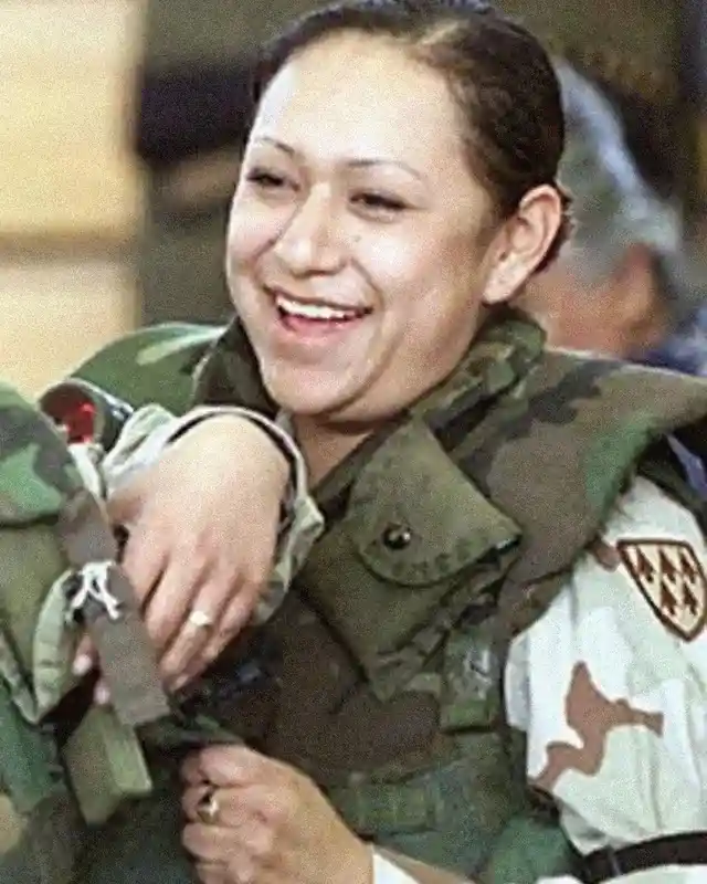a woman in military uniform, smiling broadly while holding a rifle, with overlaid text reading 'i'm not a soldier, i'm a…