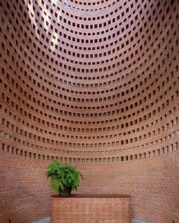 A photo of a curved, multi-tiered brick structure with a potted plant on a pedestal at the bottom. The overlaid text reads…